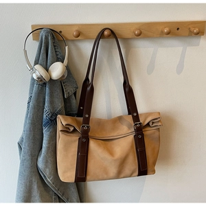 Detail of camel suede tote bag with brown leather straps hanging on a wooden hook