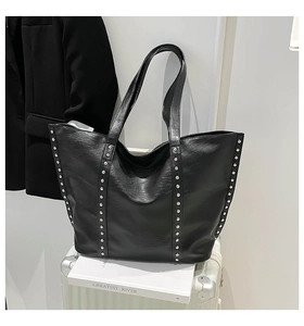 Detail of black leather tote bag with silver studs on a white suitcase background