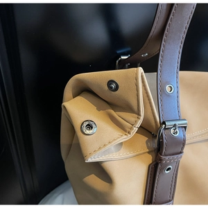 Detail of tan suede tote bag featuring brown leather straps and silver star engraved buckle