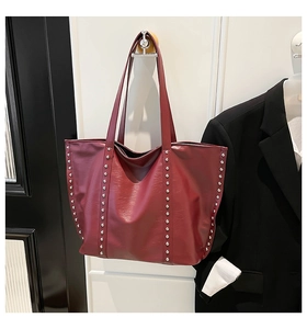 Detail of burgundy tote bag with silver rivets hanging on wall with a black blazer