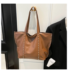 Close-up of caramel brown tote bag with silver metal rivets hanging on a wall hook