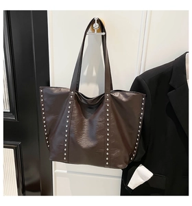 Detail of dark brown tote bag with silver rivets hanging on a white door