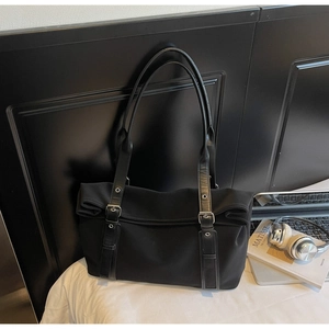 Detail of black tote bag with silver adjustable buckles and grommets on leather straps