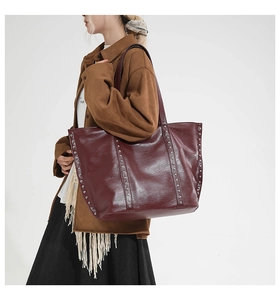 Detail view of burgundy tote bag with vertical rivet studs and smooth leather texture