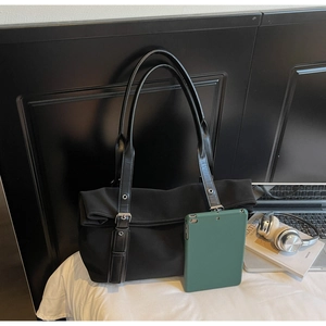Detail view of large black tote bag with leather straps and silver buckles on a bed