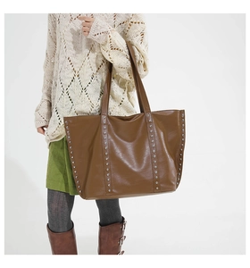 Detailed view of brown faux leather tote bag featuring stylish silver rivets and long handles
