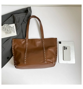 Brown rivet tote bag detail showing stud decor next to a tablet for size reference