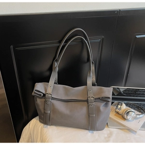 Grey matte tote bag with adjustable buckle straps shown with a laptop and book