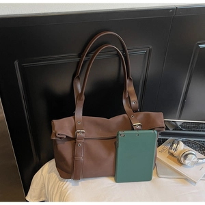 Detail of brown tote bag with double straps, flap closure and metal buckle hardware