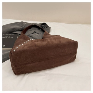 Detail view of brown matte leather shoulder bag with silver rivet studs on textured fabric