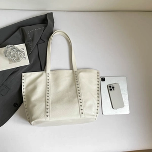 White textured leather tote bag with silver rivets and dual straps on minimalist desk
