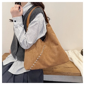 Detailed shot of brown suede tote bag featuring silver studs and leather shoulder strap