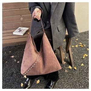 Close-up of brown suede shoulder bag featuring silver metal rivets and chic slouchy design