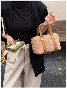Detail of beige plush Boston bag with leather handles and green wallet on a park bench
