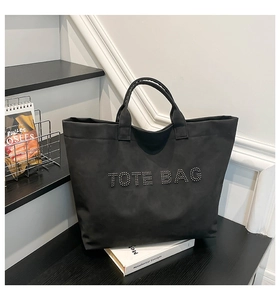 Detail of silver rivets spelling TOTE BAG on black minimalist suede finish handbag