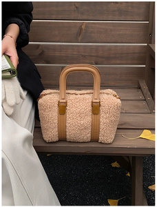 Detail of camel plush Boston bag with leather handles and gold buckles on wooden bench