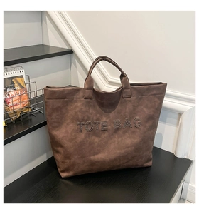 Detail of vintage brown tote bag with silver metal rivets spelling TOTE BAG on front