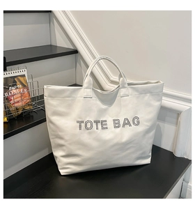 Detail of white PU tote bag with black rivet studs spelling TOTE BAG on smooth leather