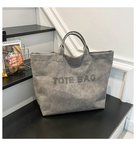 Detail shot of the matte grey tote bag featuring rivet-embellished TOTE BAG lettering