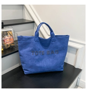 Close-up of blue tote bag with metallic stud lettering on modern display steps