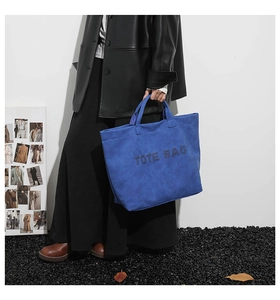 Detail of royal blue suede tote bag showing perforated TOTE BAG text and stitching