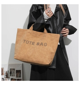 Brown suede tote bag with perforated lettering shown on a model in a black leather jacket