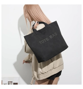 Detailed view of black tote bag with rivet TOTE BAG lettering held by a model