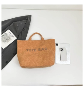 Flat lay of large brown PU tote bag with rivet text detail beside a gray blazer