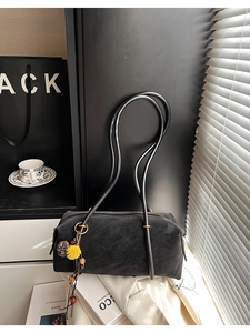 Détail du sac baguette en daim noir avec breloque fleur en peluche et boucles dorées