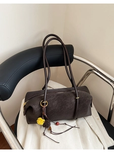 Gros plan détaillé du sac baguette cylindrique marron foncé sur un fauteuil en cuir