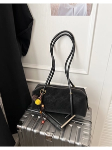Détail du sac hobo en daim noir sur valise métallique avec pendentif pompon bicolore