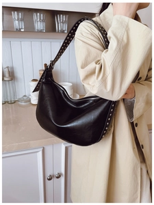 Detail of black Hobo bag with silver studs worn by a model in a beige trench coat