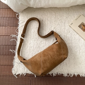 Top view of brown suede crescent bag with white stitching on a white fringe rug