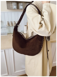 Detail of dark brown suede hobo bag with silver rivets worn over a beige trench coat