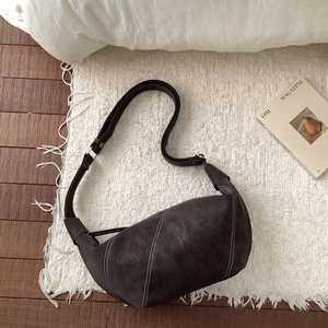 Macro detail of dark brown leather crescent bag featuring white contrast stitching accents