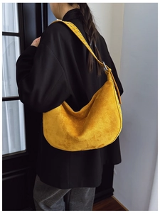 Detail of yellow suede shoulder bag with metallic grommets shown on model's shoulder