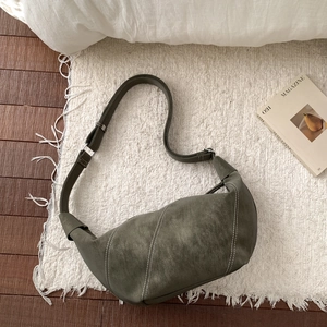 Detail of olive green crescent crossbody bag with white stitching on soft carpet