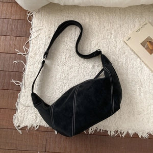 Detail of black suede hobo bag with contrast white stitching on a textured rug