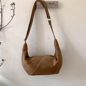 Close-up of brown leather crescent bag with white stitching detail hanging on a hook