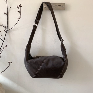 Detailed close-up of dark brown crescent bag with white contrast stitching and silver buckle