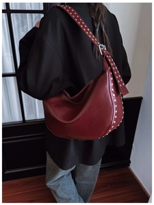 Deep red hobo bag with silver rivets and adjustable strap shown on shoulder