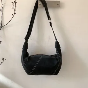Detail of black crescent crossbody bag with white contrast stitching and adjustable strap