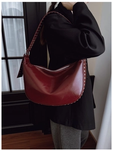 Detail of dark red hobo bag with silver studs and polished oil-wax finish on the shoulder strap