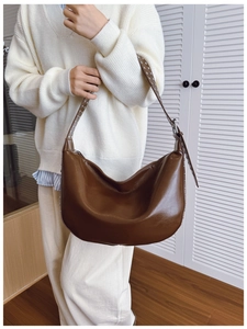 Detail view of a brown glossy leather crescent bag with studded wide shoulder strap