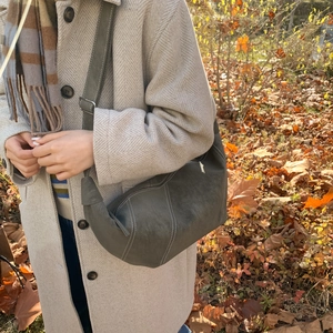 Detail of grey crescent shoulder bag with white contrast stitching in outdoor autumn setting