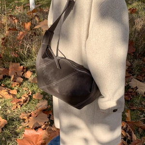 Detail of dark brown leather crescent bag with white contrast stitching on beige coat