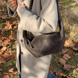 Detail of dark brown croissant hobo bag with contrast stitching on woman's coat