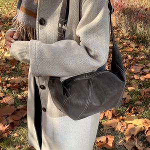 Detail of a dark brown crescent bag with white contrast stitching and wide shoulder strap