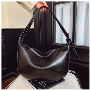 Close-up of silver rivet studs on adjustable strap of a black leather crescent shoulder bag