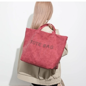Large red suede tote bag with TOTE BAG rhinestone lettering carried by a model